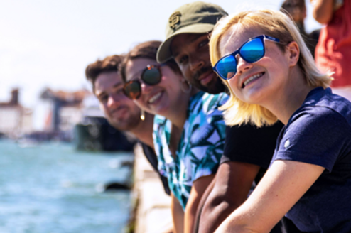 Summer students smiling on Venice canal wall.